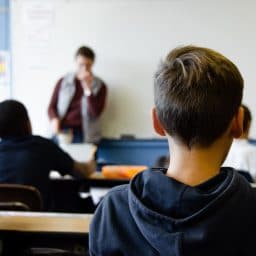 Children learning together in a classroom while a teacher stands up front.