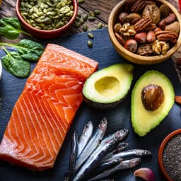 Healthy eating: high angle view of a group of food with high levels of Omega-3 fat. The composition includes salmon, sardines, avocado, extra virgin olive oil, and various nuts and seeds like pumpkin seeds, chis seeds, pecan, almonds, pistachio, walnuts and hazelnuts.