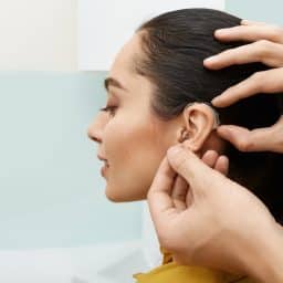 Installation hearing aid on woman's ear at hearing clinic, close-up, side view. Deafness treatment, hearing solutions