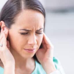 Woman with somatic tinnitus holding her ears and looking pained.