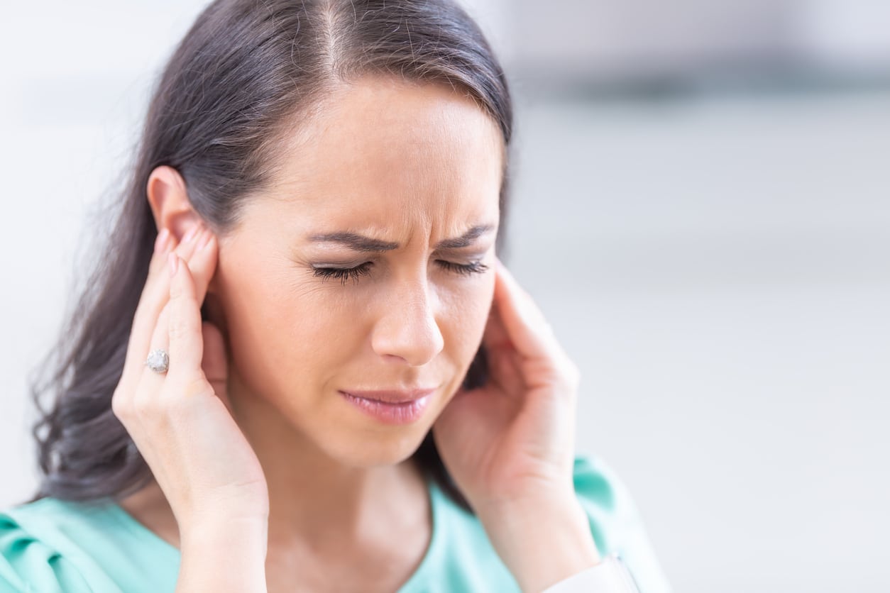 Woman with somatic tinnitus holding her ears and looking pained.