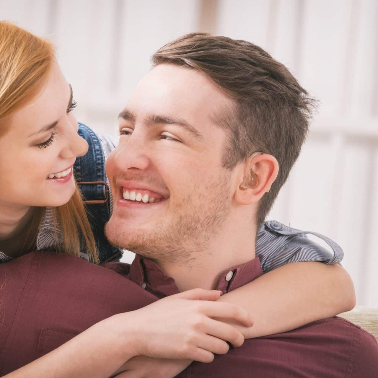 happy man smiling at his partner, her arms are around him - a hearing aid is prominently visible in his ear