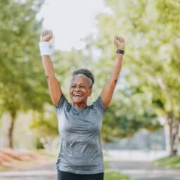 Athletic woman running through a park, excited with her arms up.