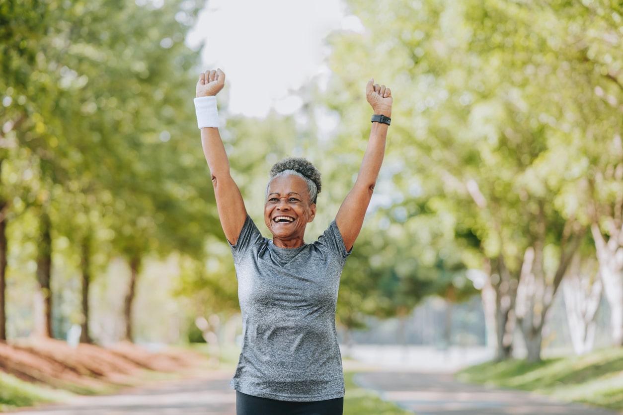 Athletic woman running through a park, excited with her arms up.