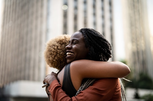Friends hugging on a street corner, big smiles