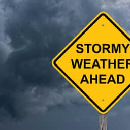Road sign reading "STORMY WEATHER AHEAD" with a stormy sky behind