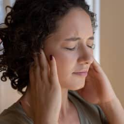 Distressed person with tinnitus covering her ears