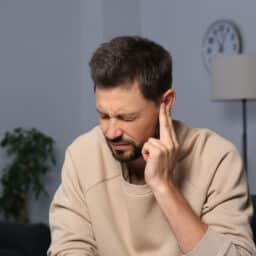 Man suffering from ear pain on in room