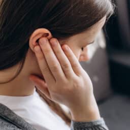 Close up of young brunette female holding painful ear, suddenly feeling strong ache in ear.