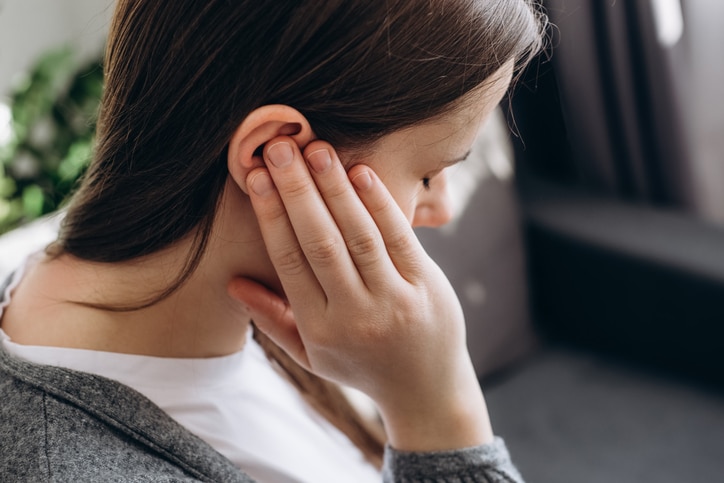 Close up of young brunette female holding painful ear, suddenly feeling strong ache in ear.