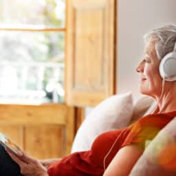 Shot of a mature woman sitting on her sofa listening to music on a digital tablet